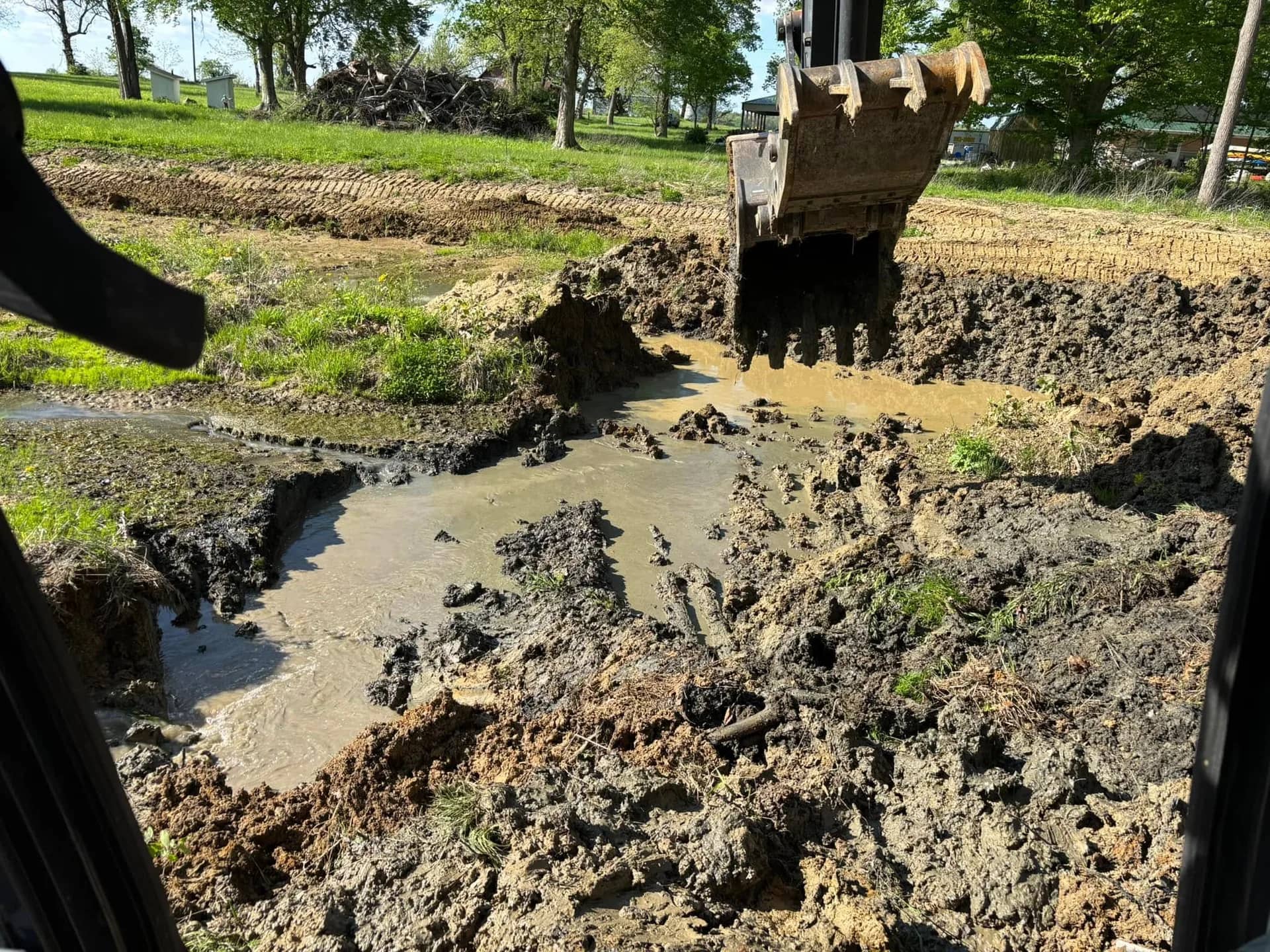 Excavator bucket pulling dark muck out of a silted pond