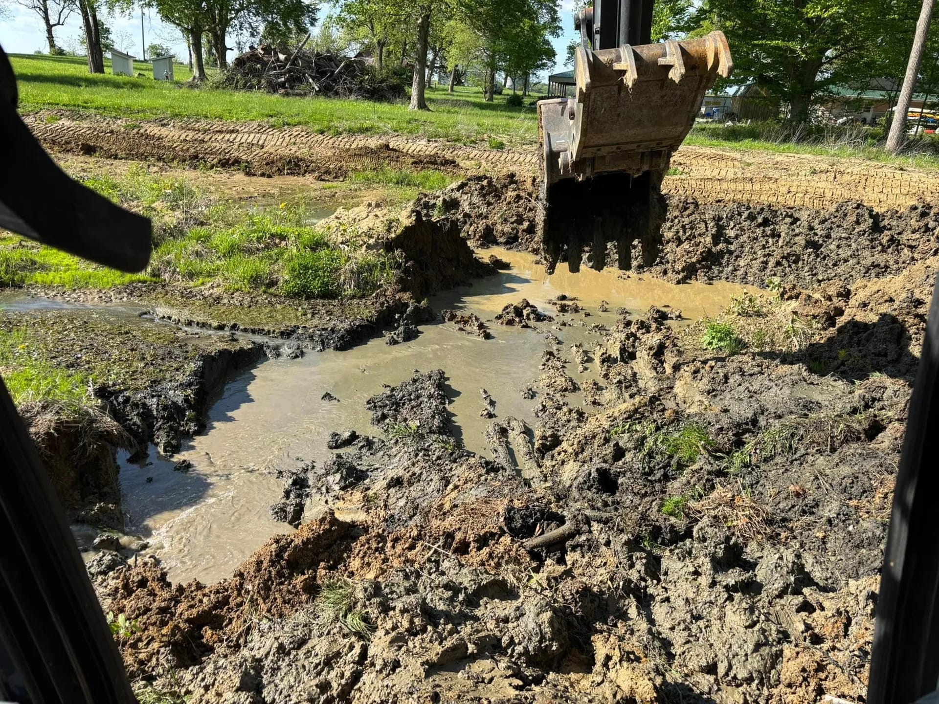Excavator bucket pulling dark muck out of a silted pond