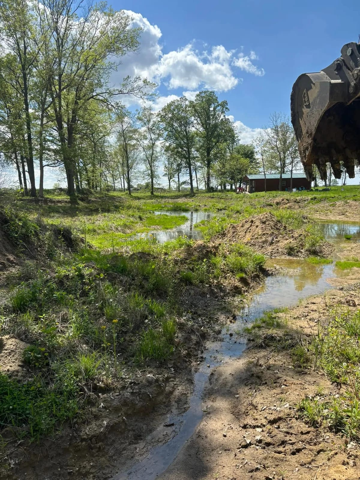 Excavator bucket raised over a silted ditch and pond inlet
