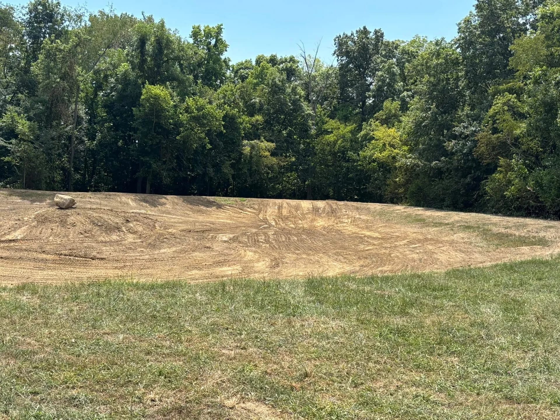 Freshly graded pond basin with a dozer parked at the tree line on a west central Indiana farm