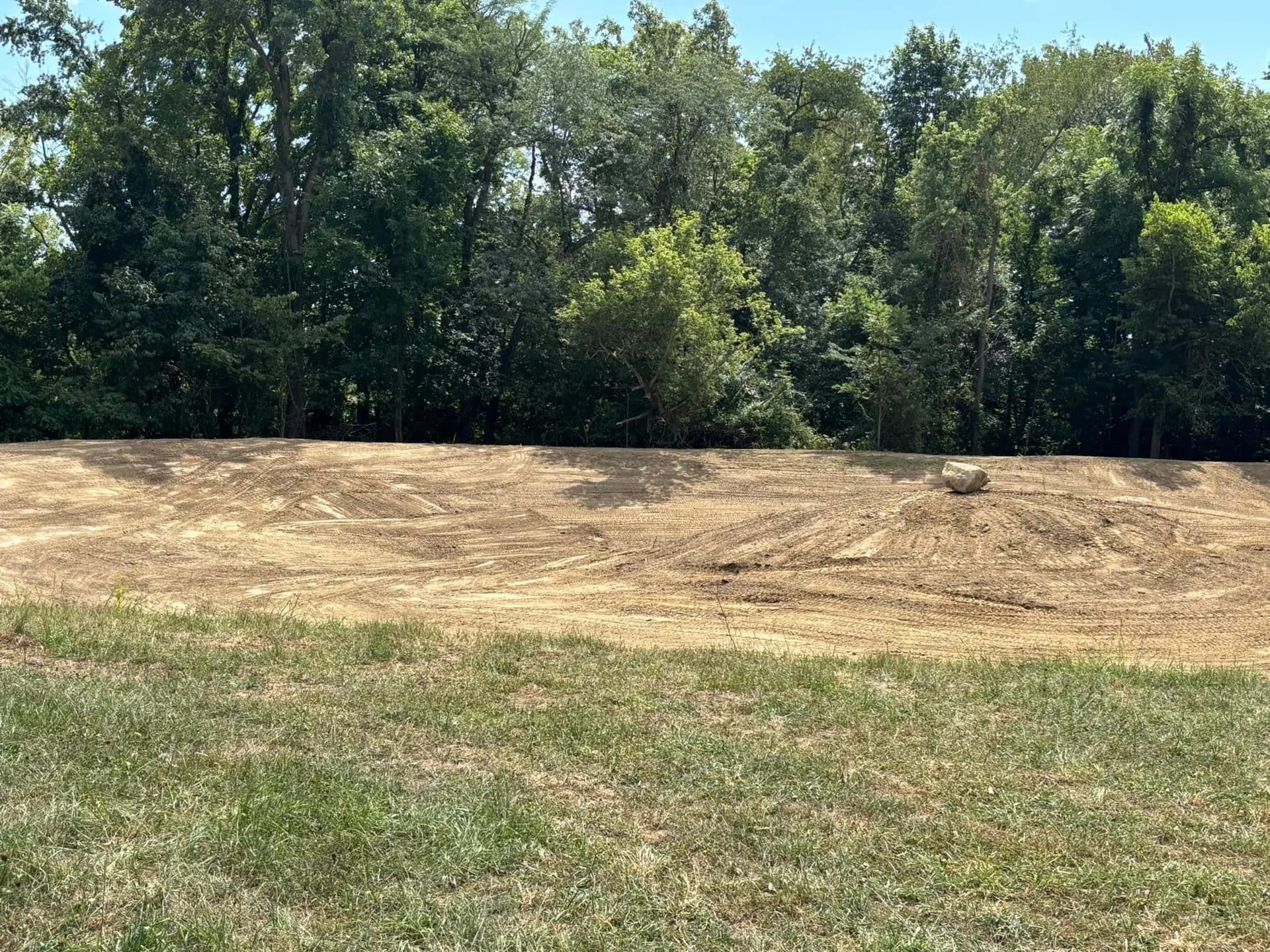 Wide view of a rough-graded site with the tree line behind