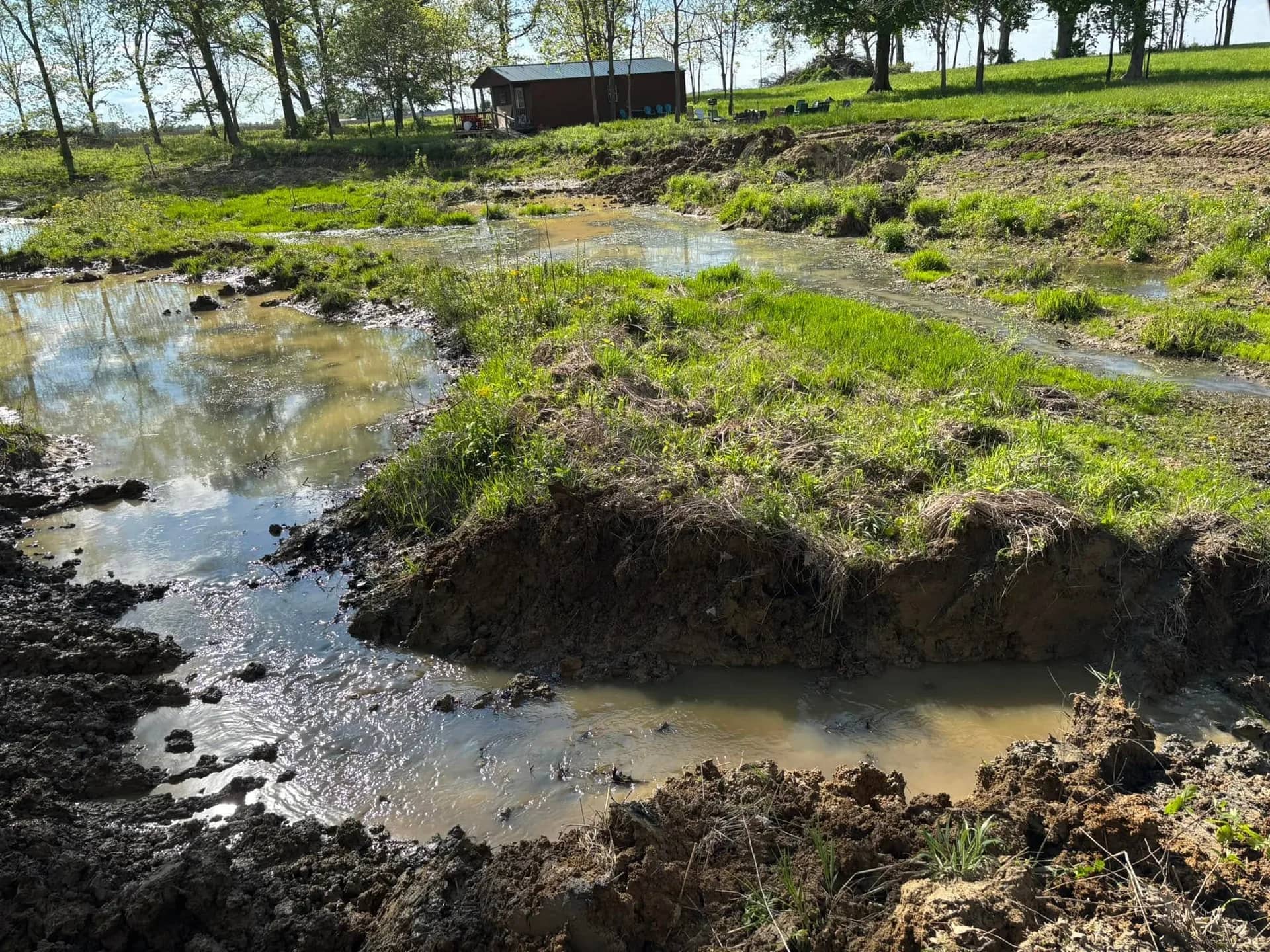 Silted pond channel being dredged, with spoil piled on the bank